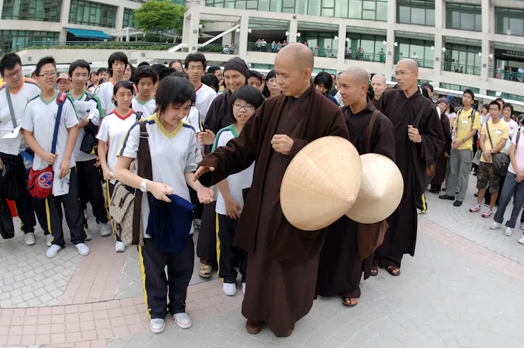 Monks in maroon robes stand in a line around schoolchildren.