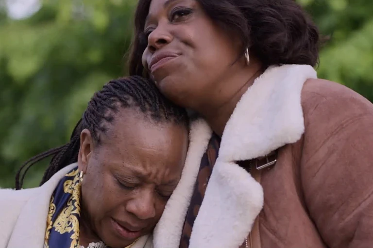 Two black women, one comforting the other is upset.