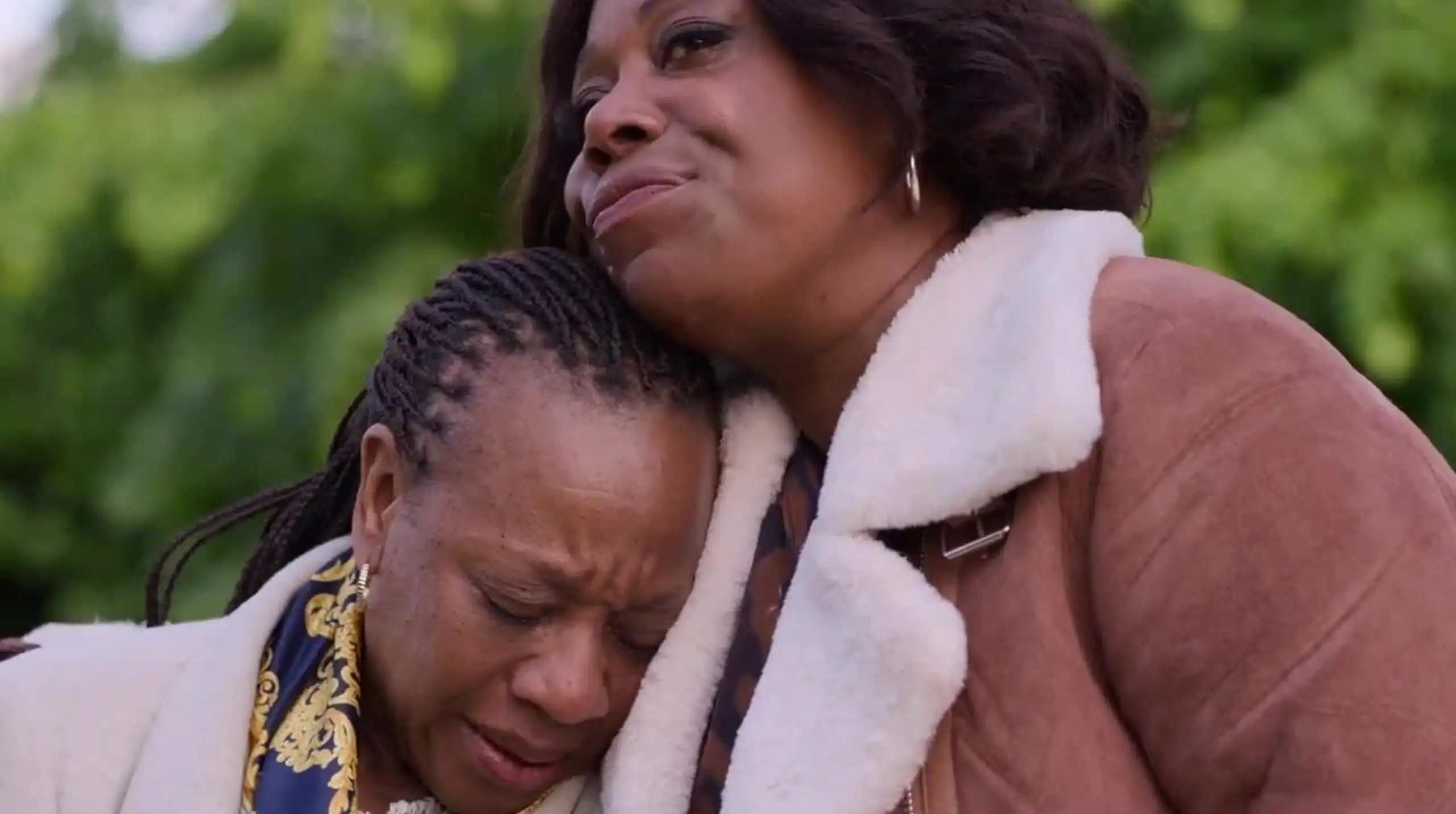 Two black women, one comforting the other is upset.
