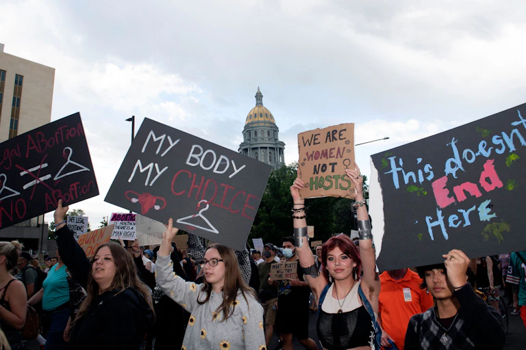 People protest in favor of abortion access, with a domed building in the background.