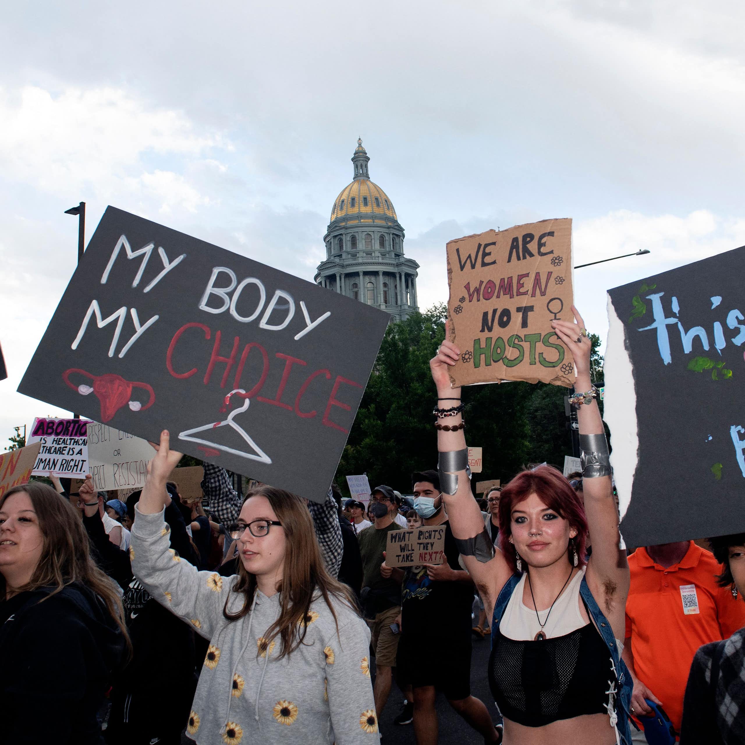 People protest in favor of abortion access, with a domed building in the background.