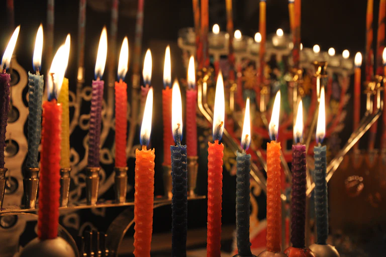 Several golden lamp-stands full of lit, colorful candles against a dark background.