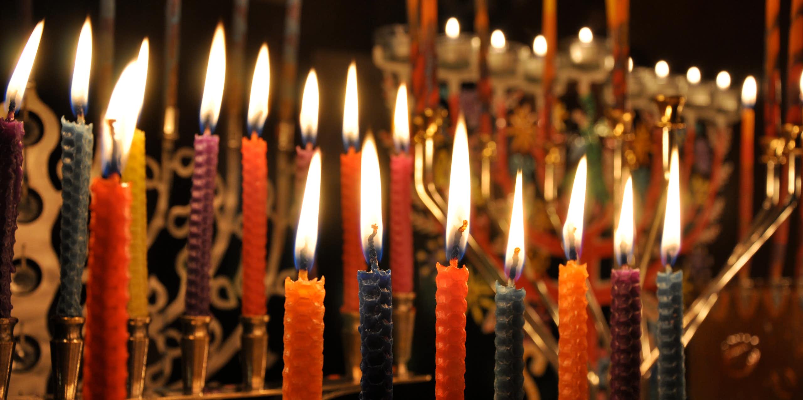 Several golden lamp-stands full of lit, colorful candles against a dark background.