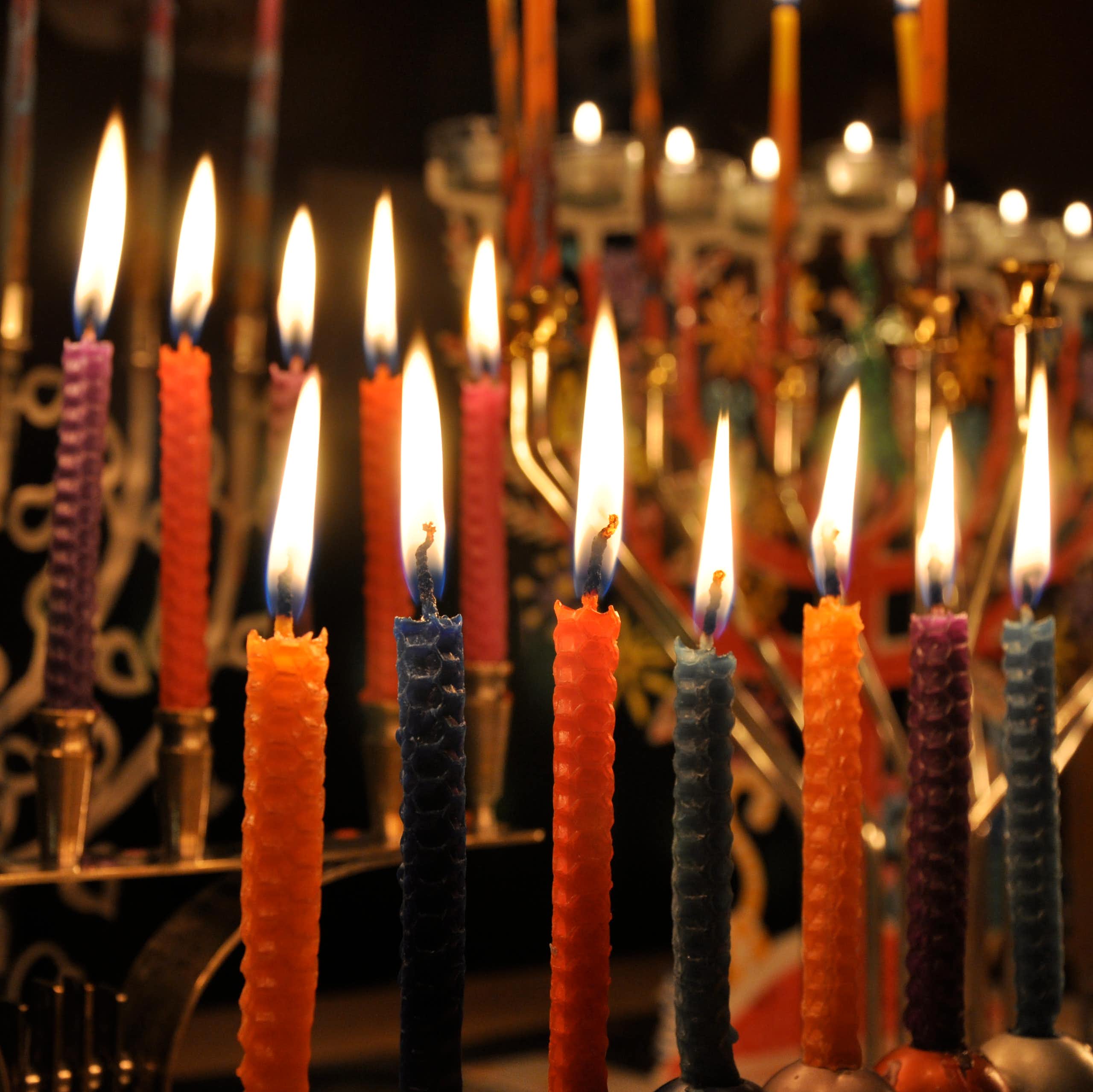 Several golden lamp-stands full of lit, colorful candles against a dark background.