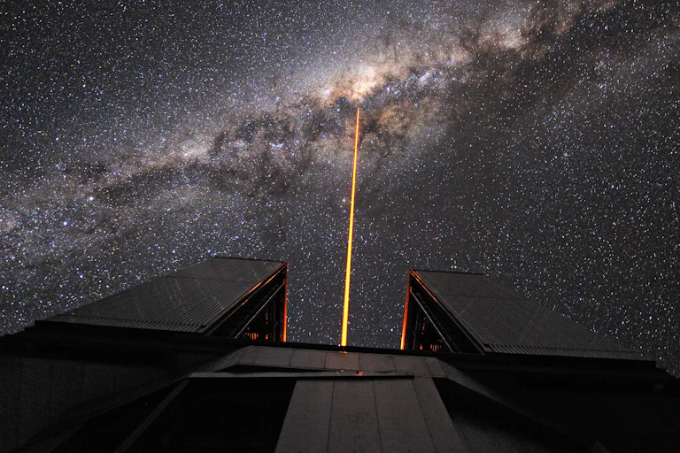 A telescope shoots an orange laser beam into a galaxy.
