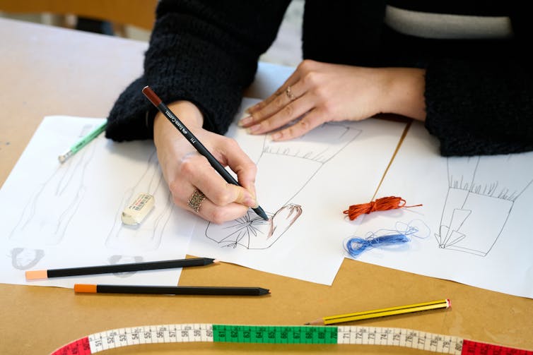 A person, seen from the shoulders down, colours in the sketch of a dress
