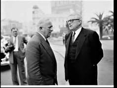 A black and white shot of two men in suits talking