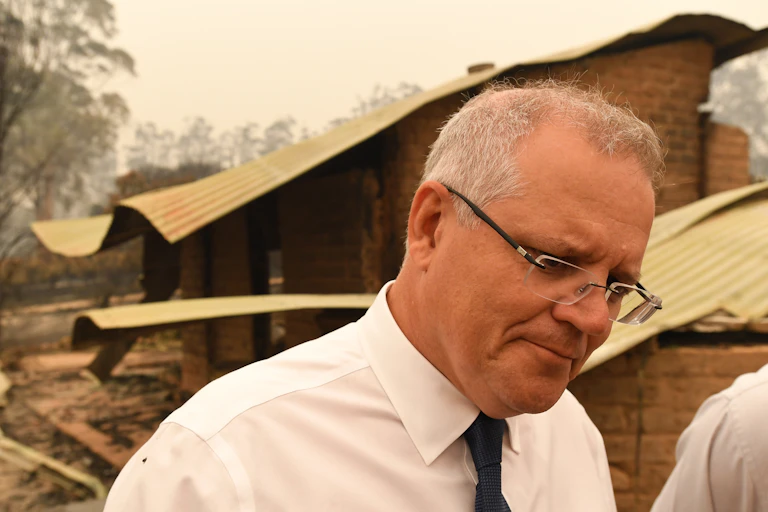 Scott Morrison looking downcast and frowning at a bushfire scene