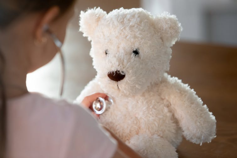 A girl's hand places a stethoscope on a white bear.