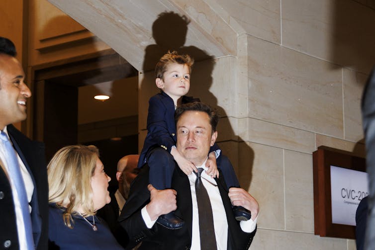 Man wearing a suit carrying a child on his head while walking through a stone building.