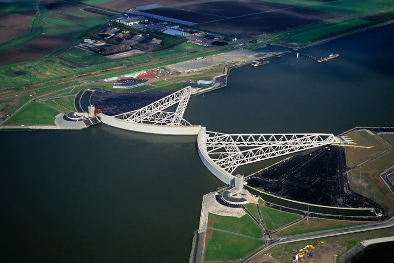 aerial shot of river mouth with flat farmland, white engineered storm barrier across river