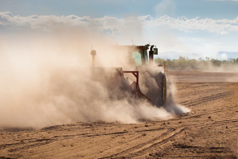 Tractors hurl up dust in a dry field.