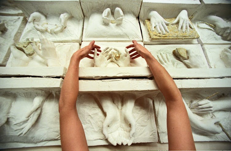 A woman's hands seen working on a piece of plaster of Paris sculpture of women's hands.