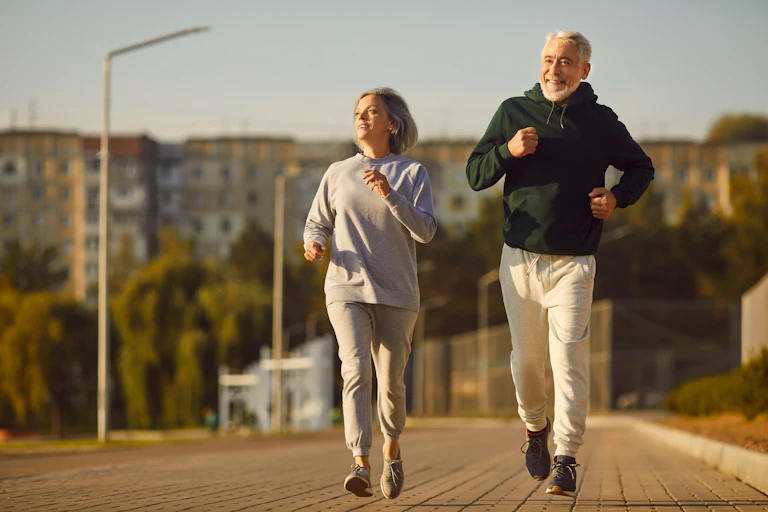 An older couple go for a run outdoors on a sunny day.