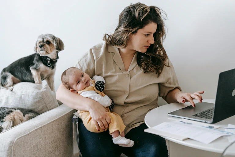 Une maman travaille à l'ordinateur avec son bébé dans les bras.