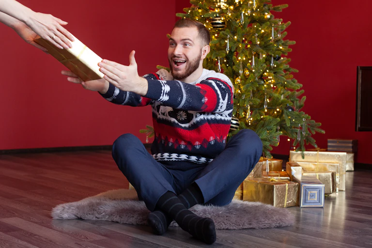 Happy man receiving gift next to Christmas tree.