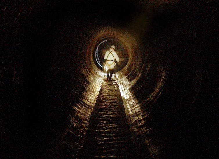 man in hi-vis walking away from camera in underground brick sewer