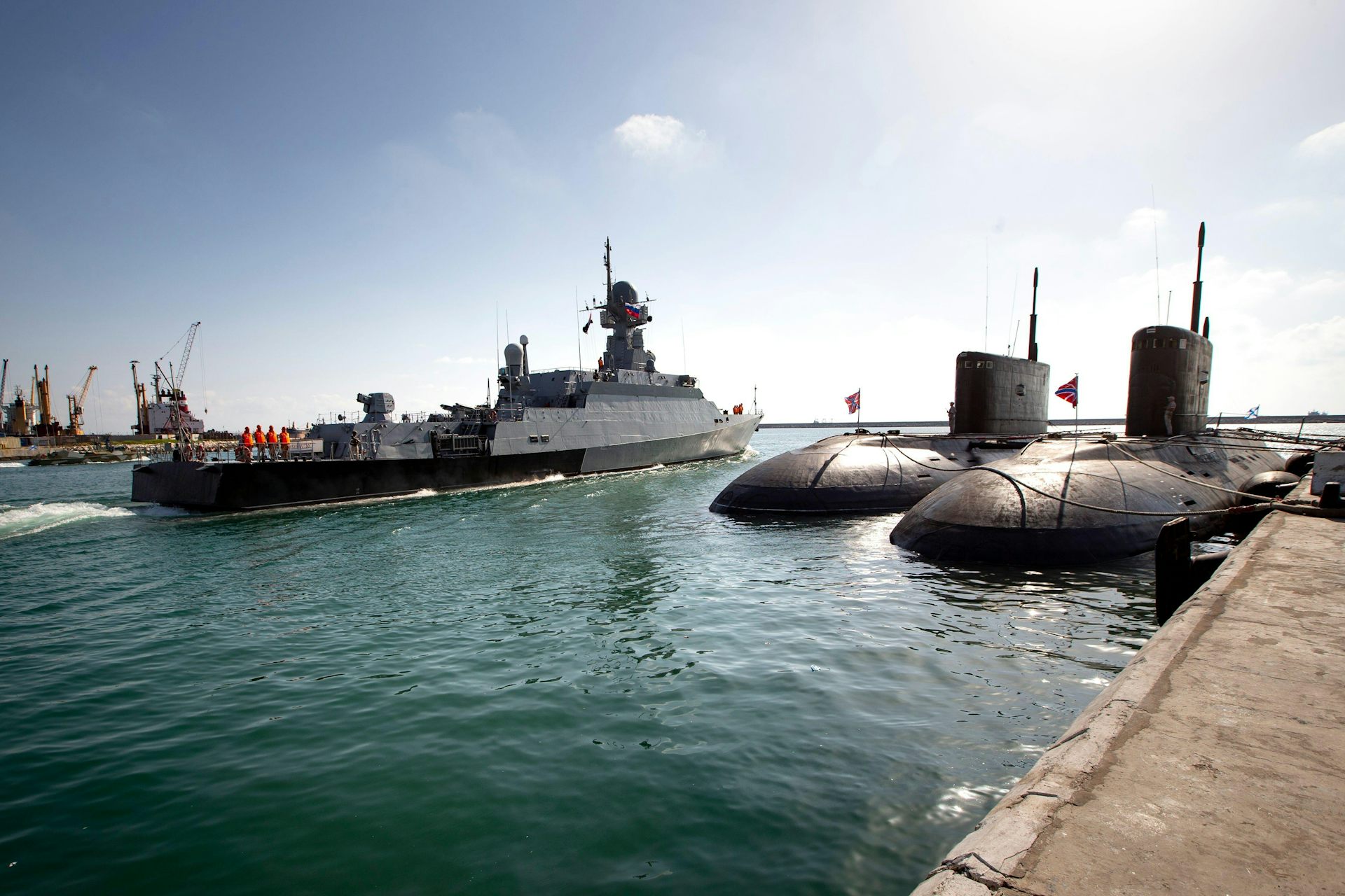 Two Russian mini-subs sit at anchor as a Russian missile ship sails out of Tartus naval base.
