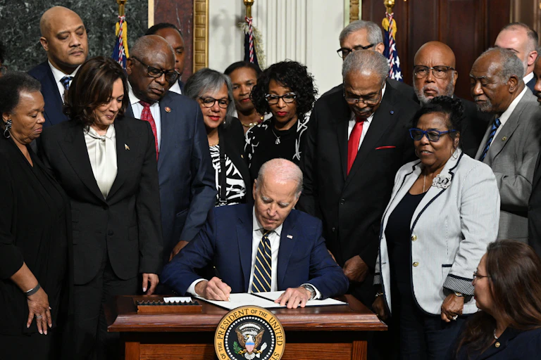 Joe Biden signe un document sur une table entouré d'un groupe de personnes