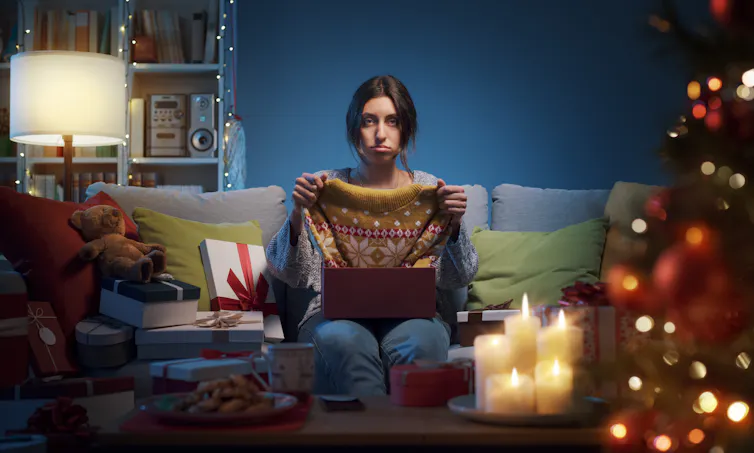 Disappointed woman holding up gifted sweater.
