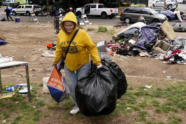 A woman carries her belongings in trash bags with destroyed tents visible in the background