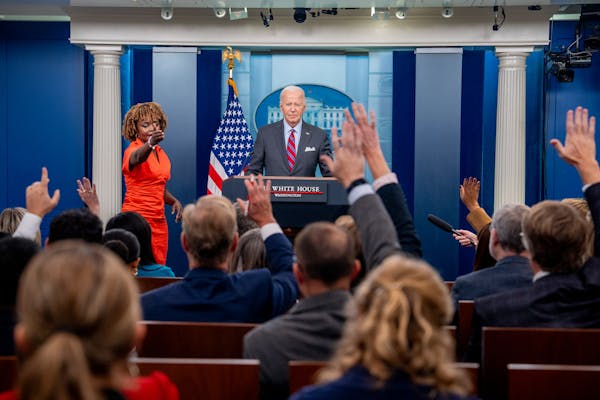 President Biden stands at the podium in the White House press room as reporters raise their hands