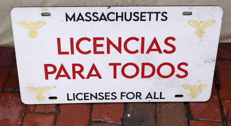A white license plate reads 'Massachusetts: licenses for all' in both English and Spanish.