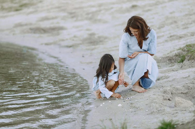 A woman and her daughter collect sea shells on the sea shore.
