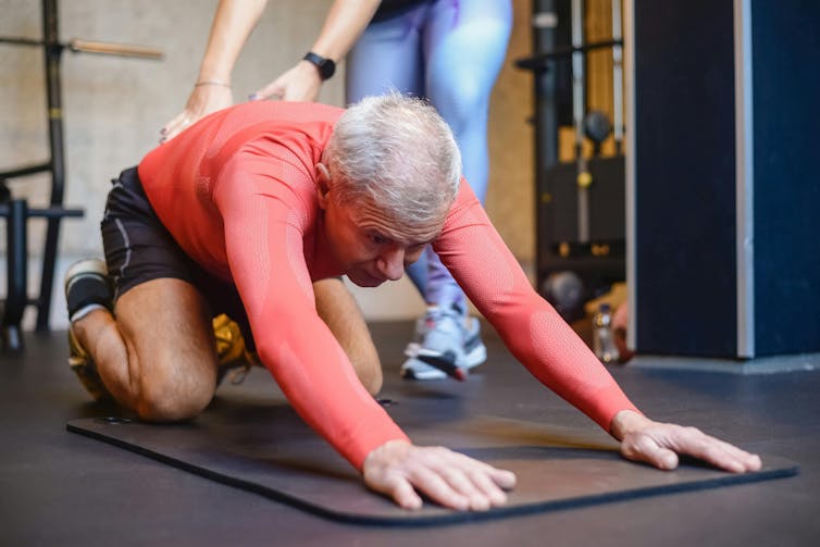 Man stretches while his pilates instructor repositions his back
