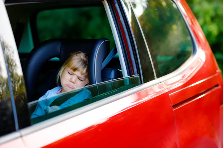 A young child sits in a carseat, pouting.