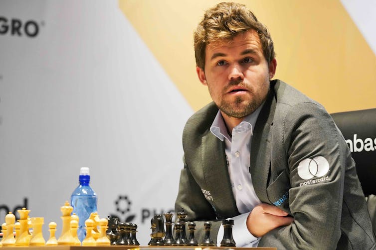 Photo of a man sitting at a chessboard.
