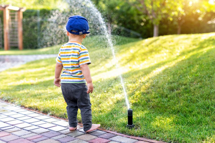 A boy standing in front of a sprinkler.