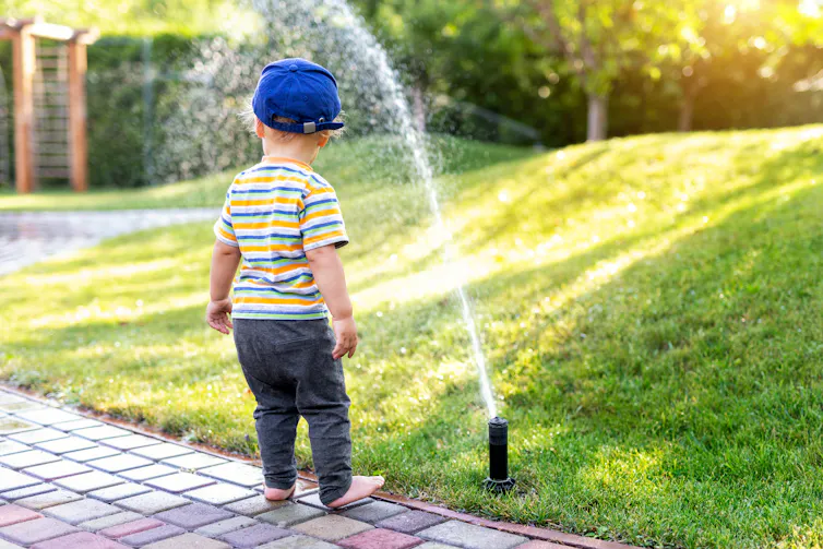A boy standing in front of a sprinkler.