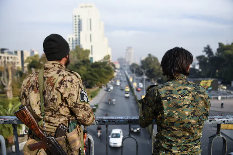 Two armed men keep watch over a road.