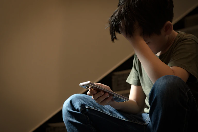 un adolescent assis dans un escalier consulte un téléphone, semblant accâblé.