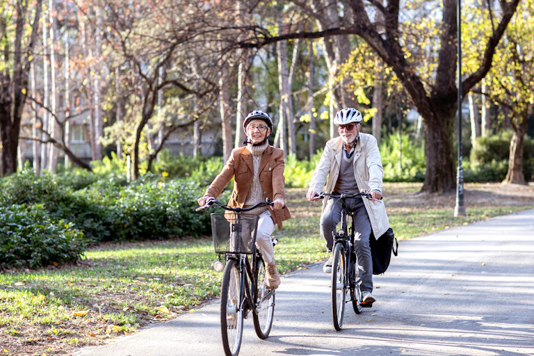 An elderly couple cycle outdoors.