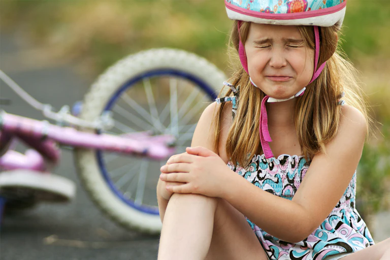 Girl holds her knee and cries after falling off bike.