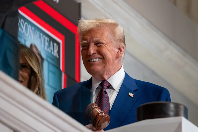 Elderly man with dyed blonde hair and a blue suit smirks.