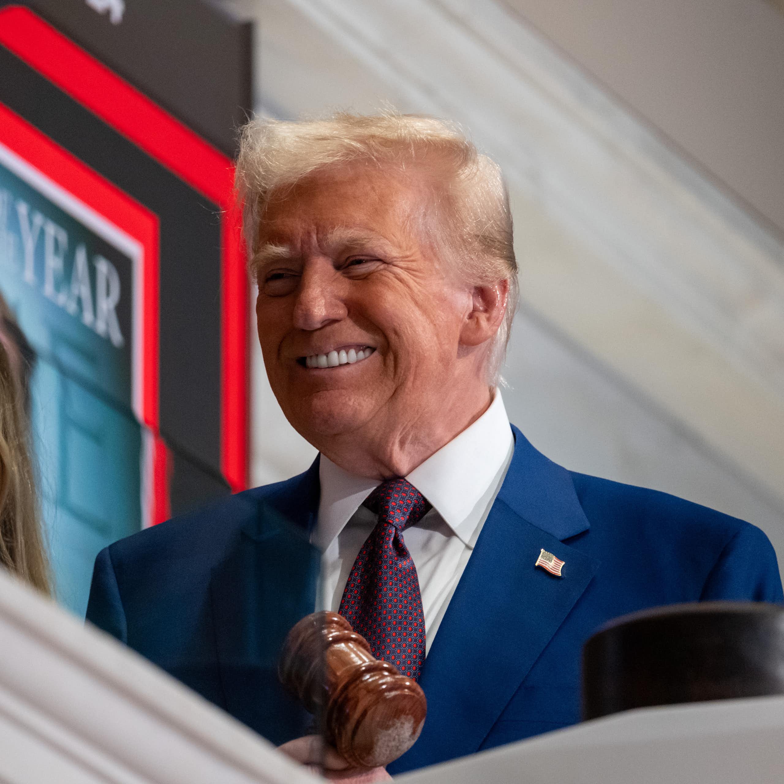 Elderly man with dyed blonde hair and a blue suit smirks.