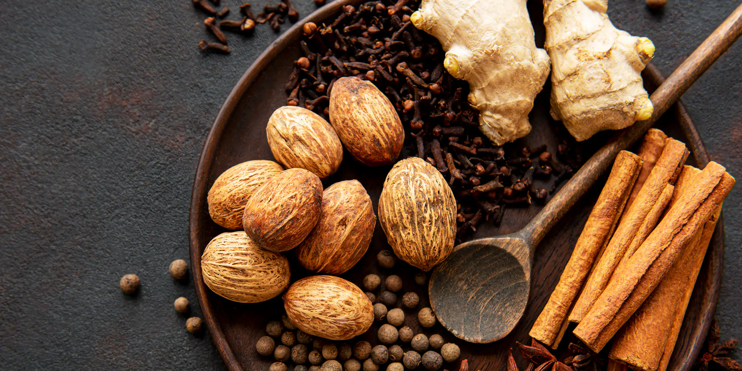 Frutos secos de nuez moscada y canela en rama, jengibre fresco y otras especias en un plato