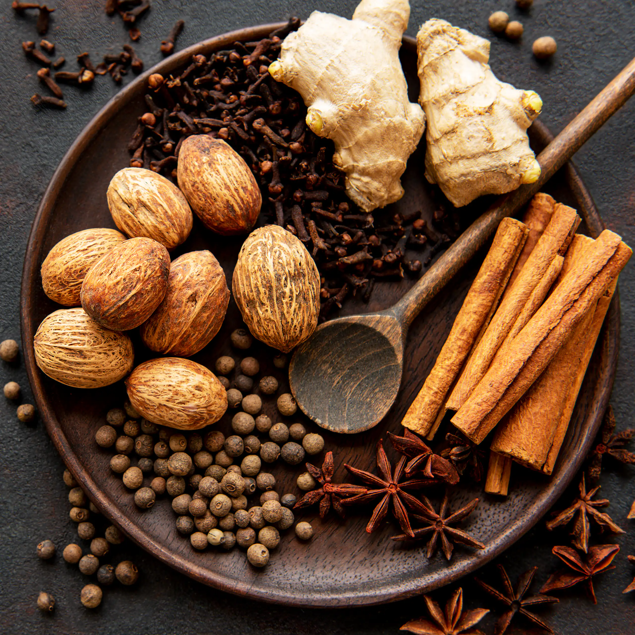 Frutos secos de nuez moscada y canela en rama, jengibre fresco y otras especias en un plato