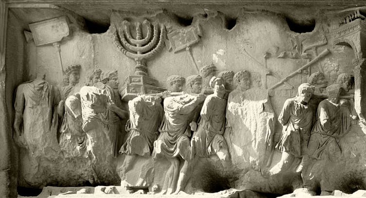A pale relief of a crowd of men in ancient Roman clothing carrying items in a procession.