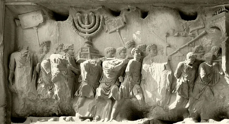 A pale relief of a crowd of men in ancient Roman clothing carrying items in a procession.