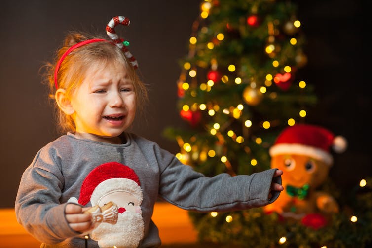 A young girl in a Christmas headband and jumper cries.