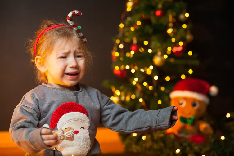 A young girl in a Christmas headband and jumper cries.