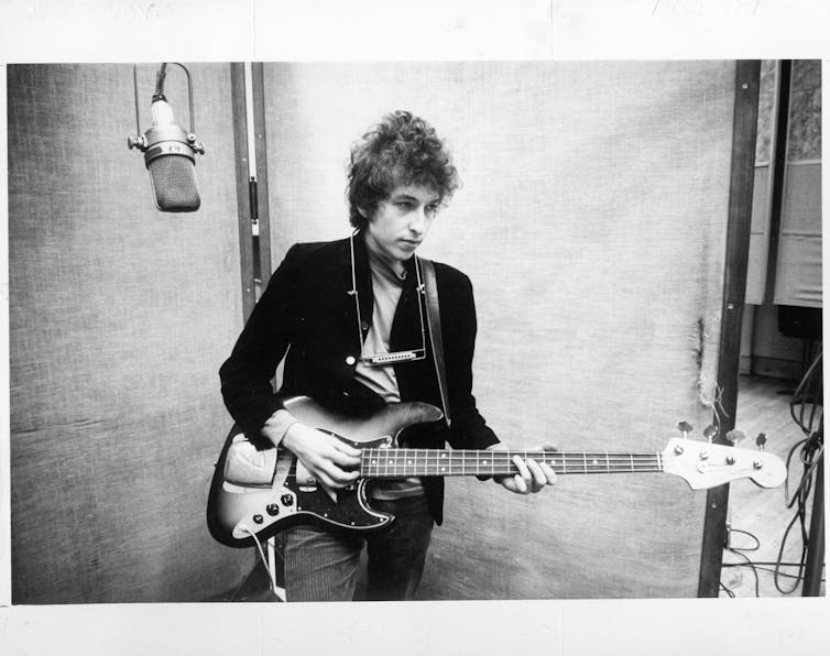 Young man places a guitar with a harmonica hanging from his neck.