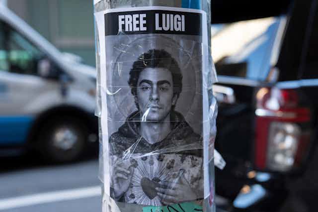 A sign featuring the face of a dark-haired young man says Free Luigi and is taped to a pole.