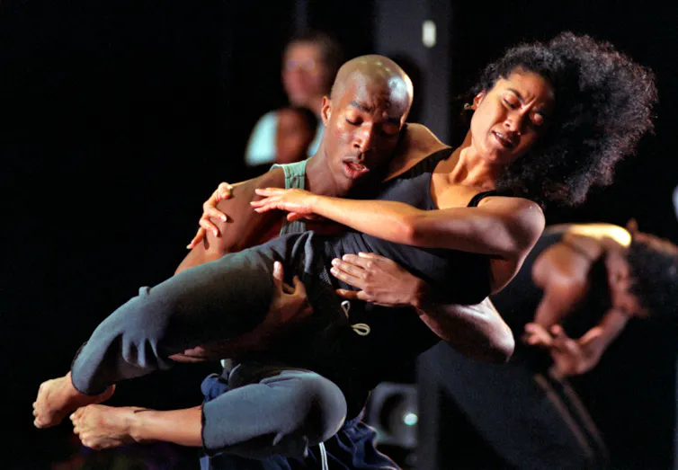 A man in a tank top lifts a woman in black pants and a black tank top as they rehearse a dance.