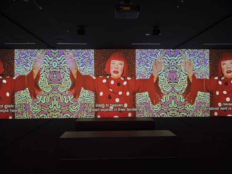 A woman in a red wig sings on a video.