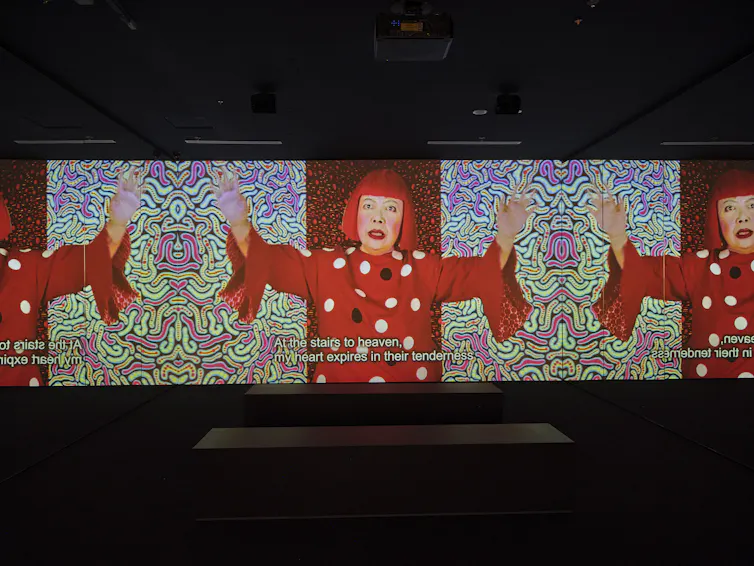 A woman in a red wig sings on a video.